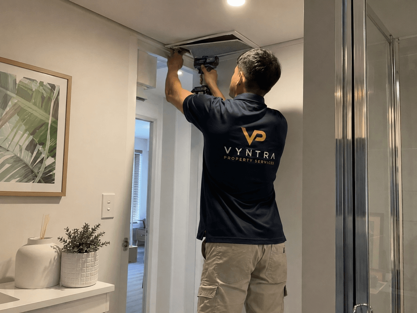 A Vyntra maintenance professional servicing a ceiling air conditioning vent